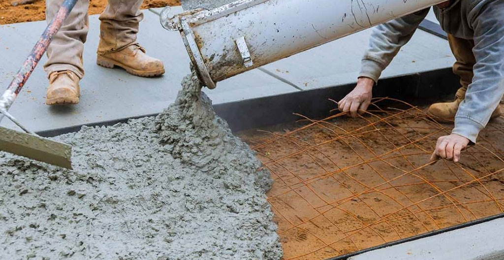 Operario agrícola visto de espaldas preparando dosificación de materiales para hormigón con sacos de cemento y áridos organizados